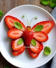 a white plate topped with strawberries and a butterfly shaped fruit decoration on top of it