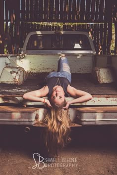 a woman laying on the back of a truck in front of a rusted pickup