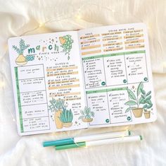 an open planner with plants on it next to a pen and some lights in the background