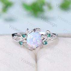 an opal ring with leaves and green stones on the side, sitting on top of a