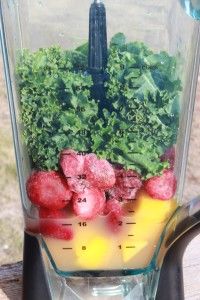 a blender filled with fruits and vegetables on top of a wooden table next to grass