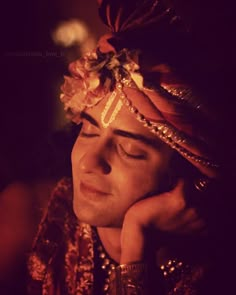 a man with his eyes closed wearing a headdress and holding his hand to his face