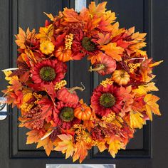 a wreath with fall leaves and pumpkins hanging on a door