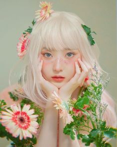 a woman with blonde hair and flowers around her neck, posing for a photo in front of a green background