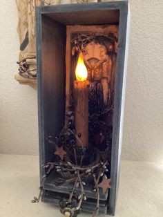 a lit candle in a wooden box with branches and star decorations on the sides, sitting next to an owl figurine