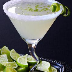 a margarita cocktail garnished with limes on a black plate and serving utensils