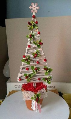 a small white christmas tree on top of a potted plant with red and green decorations