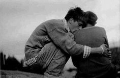 an old black and white photo of two people hugging each other in front of a fence