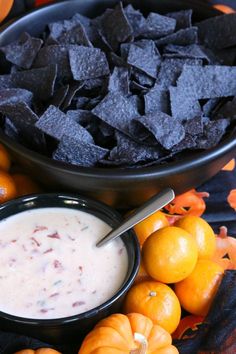 an assortment of fruit and chips on a table with oranges, guacamole, and black tortilla chips