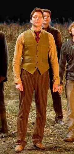 three men standing next to each other in front of a cornfield with one man wearing a vest and tie