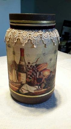 a glass jar sitting on top of a table covered in food and wine bottles with lace trim around the edges