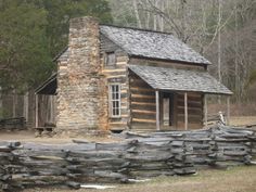 an old log cabin in the woods on a foggy day with logs piled around it