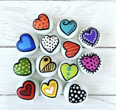 nine painted hearts are arranged in a circle on a white wooden surface with polka dots