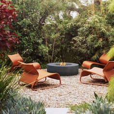 an outdoor fire pit surrounded by plants and rocks in the middle of a gravel area