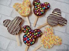 six decorated heart shaped lollipops are arranged on a white brick wall with chocolate and sprinkles