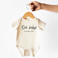 a person holding up a baby's bodysuit with the word oh baby on it