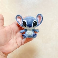 a hand holding a small crocheted blue and white stitched toy with big eyes