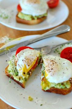 two white plates topped with sandwiches covered in an egg and tomato topping next to a fork