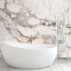 a large white bath tub sitting in front of a marble tiled wall and floor next to a towel rack