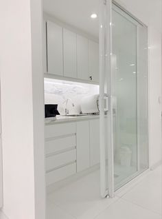 an all white kitchen with glass doors leading to the shower area and toilet in the corner