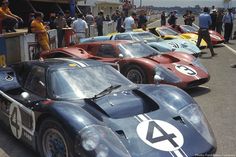 several race cars are lined up on the side of the road as people look at them