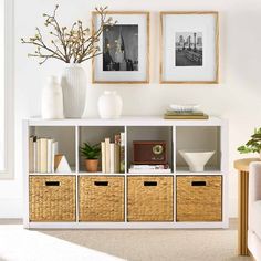 a white shelf with baskets and pictures on it next to a couch in a living room