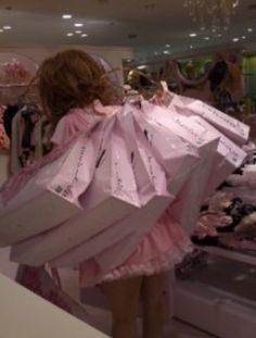 a woman in a pink dress is holding shopping bags and looking at the clothing on display