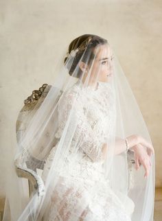 a woman in a wedding dress sitting on a chair with a veil over her head