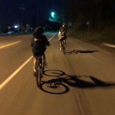 two bicyclists riding down the road at night