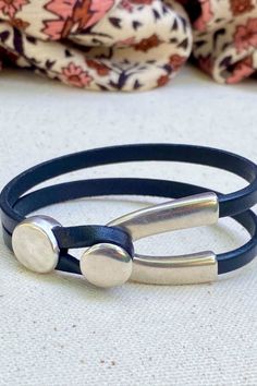 two leather bracelets with metal clasps on top of a white cloth covered surface