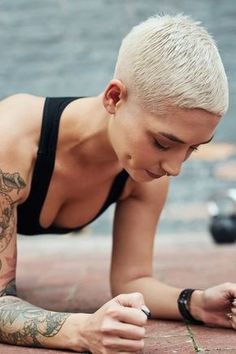 a woman with white hair and tattoos on her body laying on the ground next to a skateboard