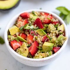 a bowl filled with strawberries and avocado on top of a white table