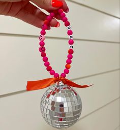 a hand holding a disco ball ornament with a red ribbon around the bead