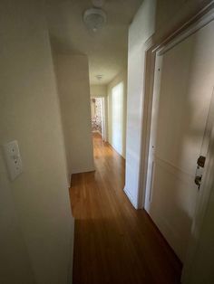 an empty hallway with hard wood flooring and light fixture on the far wall, leading to another room