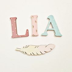 the letters are made out of wood and decorated with pastel colors, such as pink, blue, and white