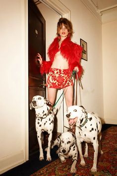 a woman with two dalmatian dogs standing in front of a door wearing a red jacket