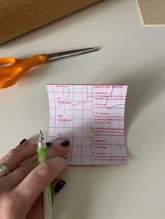 a person holding a pen near a piece of paper with scissors on top of it