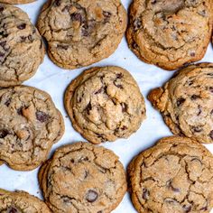 chocolate chip cookies are lined up on a sheet of parchment paper, ready to be eaten