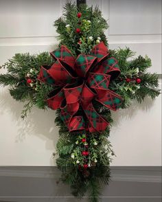 a christmas wreath hanging on the side of a door with red and green bows attached to it