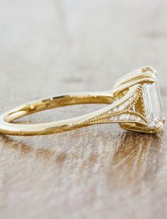 a gold ring with an emerald cut diamond in the center on a wooden table top