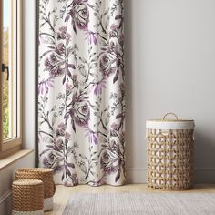 a white and purple floral shower curtain next to a window with a basket on the floor