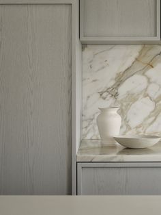 a white vase sitting on top of a counter next to a bowl in front of it