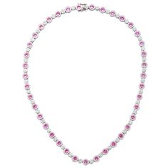 The timeless elegance of this tennis setting converges with rich pink sapphires to create a breathtakingly elegant design. Crafted in sterling silver, round-cut pink sapphires are prong set in a halo of created white sapphires with created white sapphire flower clusters connecting each pink sapphire. Glistering pink sapphires embezzle your neck with this timeless, royal design. Finished with an SL logo and a Suzy Levian Secret Signature brown diamond in the back gallery, this necklace is designe Elegant Round Gemstone Tennis Necklace, Elegant Gemstone Tennis Necklace, Luxury Pink Jewelry With Prong Setting, Luxury Pink Sapphire Round Jewelry, Fine Jewelry Pink Sapphire Round Cut, Anniversary Gemstone Tennis Necklace, Anniversary Round Gemstone Tennis Necklace, Formal Pink Diamond Necklace, Classic Silver Jewelry With Pink Sapphire