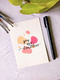 a card with some writing on it next to two pens and a potted plant