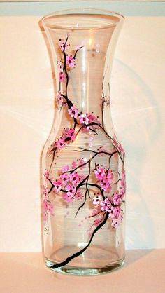 a glass vase with pink flowers painted on the side and black branches in the middle