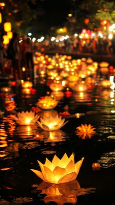 lanterns floating on the water with people standing around them in the background at night time