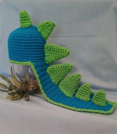 a crocheted blue and green dragon hat next to a gold starfish