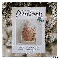 a baby's first christmas card hanging from a tree with pine cones and snow