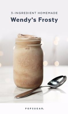 a mason jar filled with frosting next to a spoon on top of a table