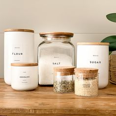 three jars with labels on them sitting on a wooden table next to a potted plant